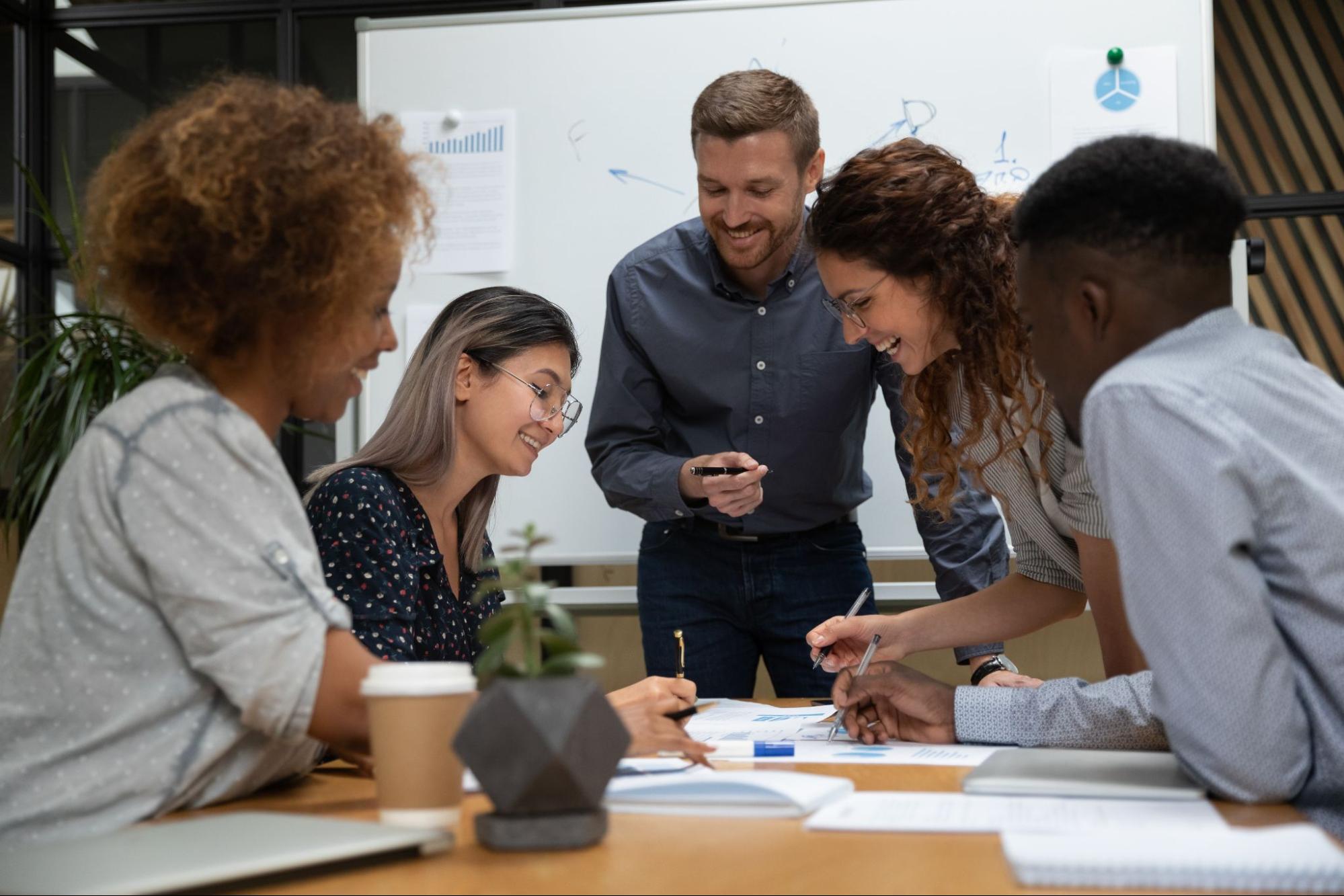 Group of employees smiling and looking over reports in front of a whiteboard